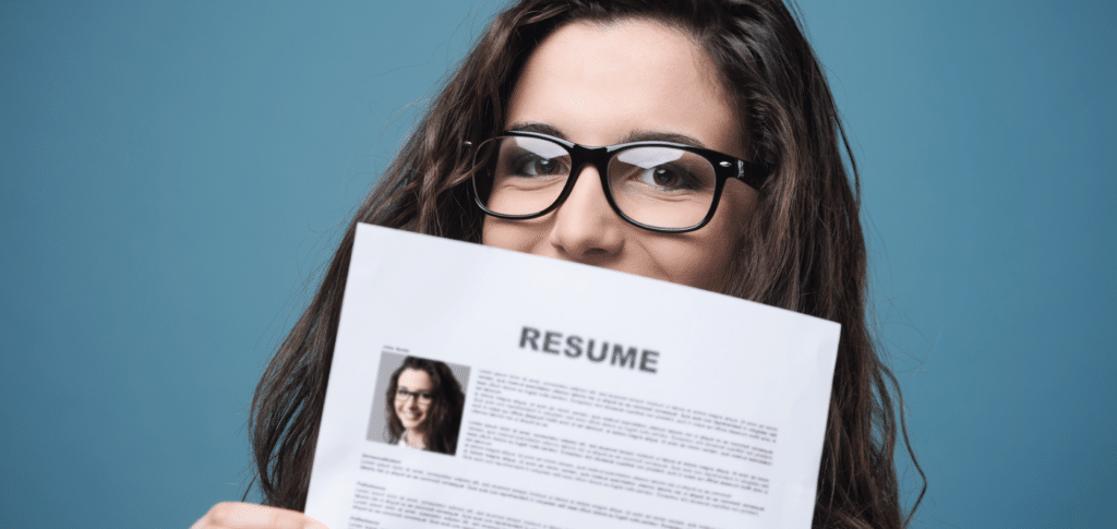 female in glasses holding printed copy of her resume in front of her face