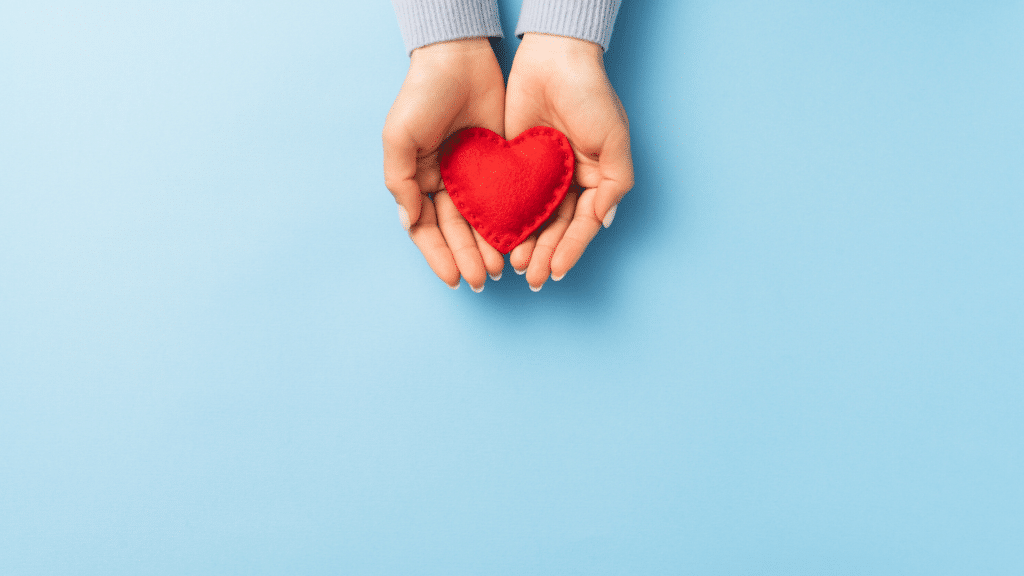 Hands holding red felt heart on a blue background