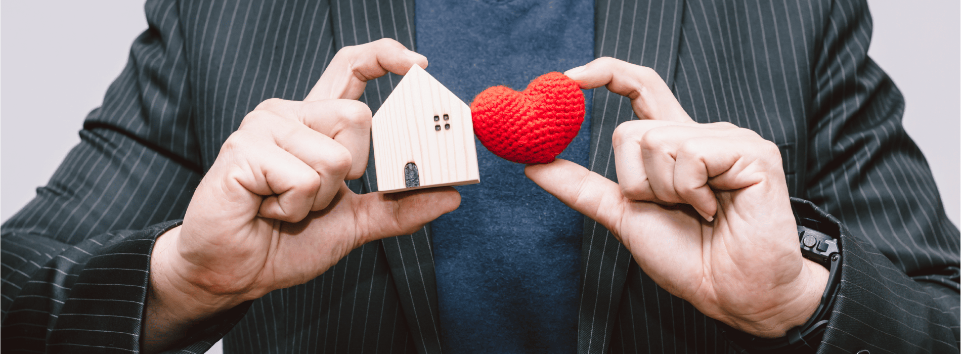 close up of a man holding a wooden house figure and heart figure in both hands