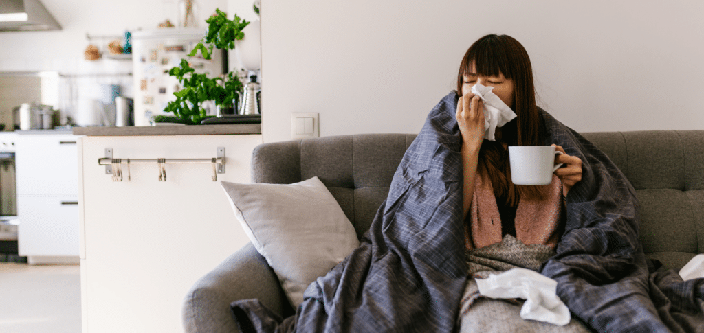 woman on couch blowing nose holding tea